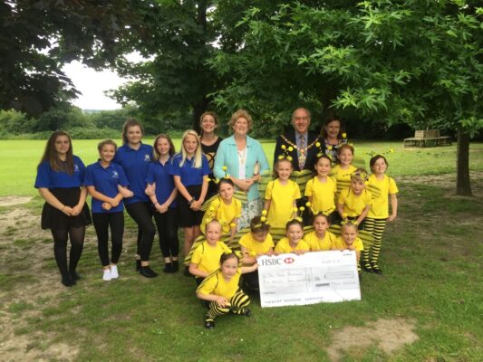 A group of adults and children with a large cheque stood in a park.
