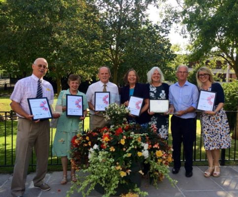 Group of people holding certificates. Container of flowers in foreground.