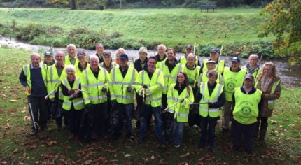 Group of people in high viz jackets with litter pickers and black sacks.