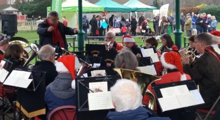 Orchestra playing in a bandstand and wearing Christmas hats.
