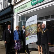 Five people standing with Farnham in Bloom sail flag outside Specsavers shop.