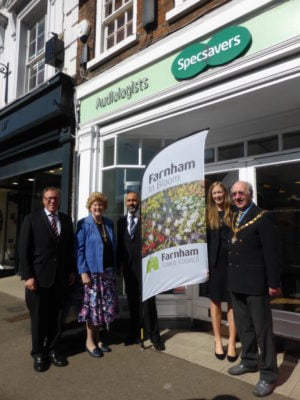 Five people standing with Farnham in Bloom sail flag outside Specsavers shop.