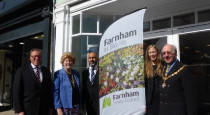 Five people standing with Farnham in Bloom sail flag outside Specsavers shop.