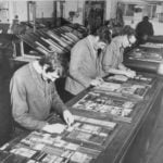 Black and white photo of three males making plates for printing