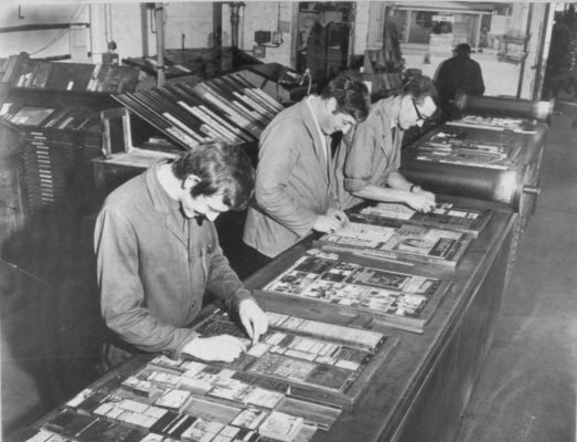 Black and white photo of three males making plates for printing