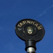 Rounded top of black iron sign post with Farnham painted in gold lettering.