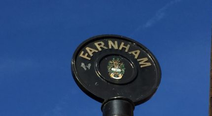 Rounded top of black iron sign post with Farnham painted in gold lettering.