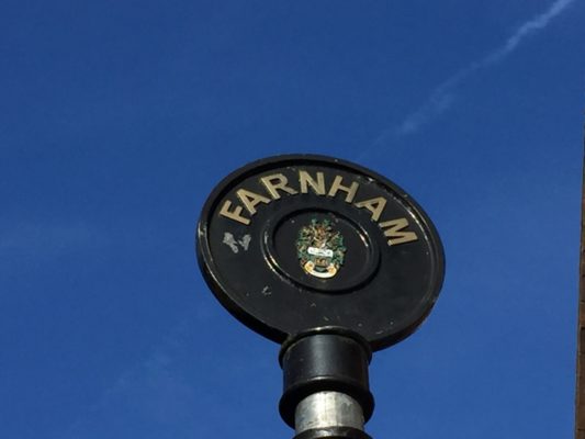 Rounded top of black iron sign post with Farnham painted in gold lettering.