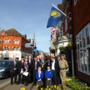 A group of people including soldiers, the Mayor and two children stand beneath Commonwealth flag.