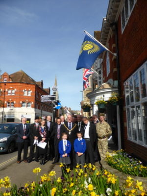 A group of people including soldiers, the Mayor and two children stand beneath Commonwealth flag.