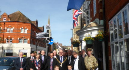 A group of people including soldiers, the Mayor and two children stand beneath Commonwealth flag.