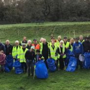 Group of people wearing high viz jackets and standing on grassy area holding blue sacks and litter pickers.