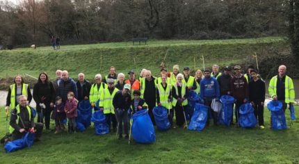 Group of people wearing high viz jackets and standing on grassy area holding blue sacks and litter pickers.