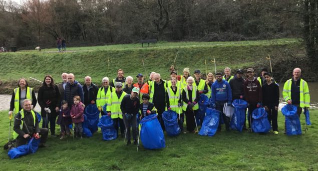 Group of people wearing high viz jackets and standing on grassy area holding blue sacks and litter pickers.