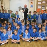 50+ school children sitting and standing in a group. Mayor holding bee keeper's suit.