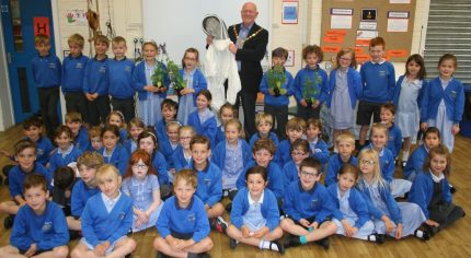 50+ school children sitting and standing in a group. Mayor holding bee keeper's suit.