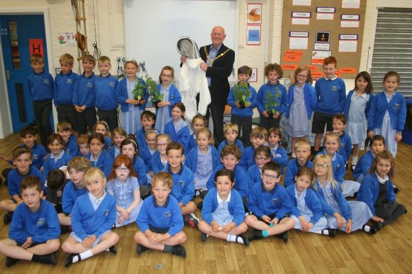 50+ school children sitting and standing in a group. Mayor holding bee keeper's suit.