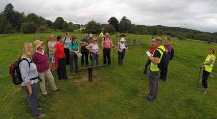 Group of walkers standing in field listening to walk guide.