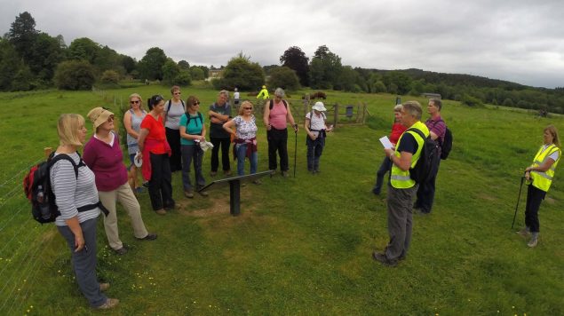 Group of walkers standing in field listening to walk guide.