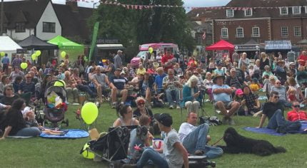 Lots of people siting on grass enjoying a music festival and picnic