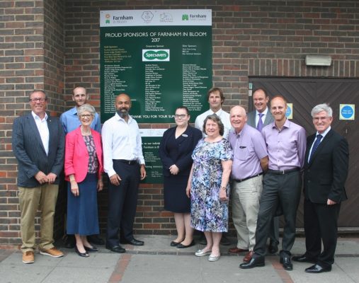 Group of people standing in front of green board showing the names of sponsors of Farnham in Bloom.