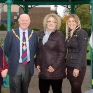 Mayor and three females in front of bandstand decorated with Christmas decorations.