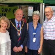 Four people (including the Mayor) standing in front of two green gazebos at a health and well-being event.