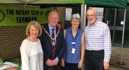 Four people (including the Mayor) standing in front of two green gazebos at a health and well-being event.