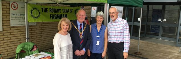 Four people (including the Mayor) standing in front of two green gazebos at a health and well-being event.