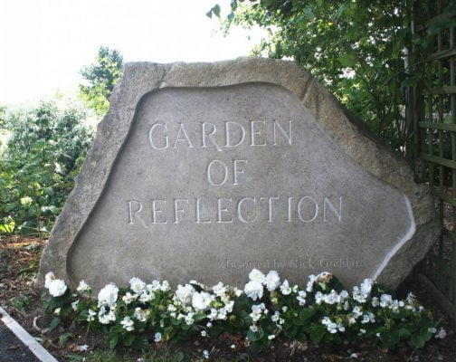 Large stone engraved with the words Garden of Reflection. White flowers at base of stone.