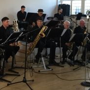 Seven piece band sitting down playing musical instruments