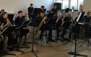 Seven piece band sitting down playing musical instruments