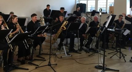 Seven piece band sitting down playing musical instruments