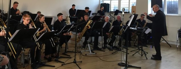 Seven piece band sitting down playing musical instruments