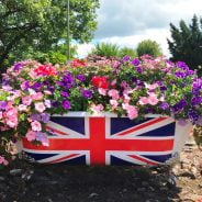 Bath tub filled with flowers and a union flag on side of bath.