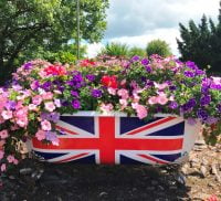 Bath tub filled with flowers and a union flag on side of bath.