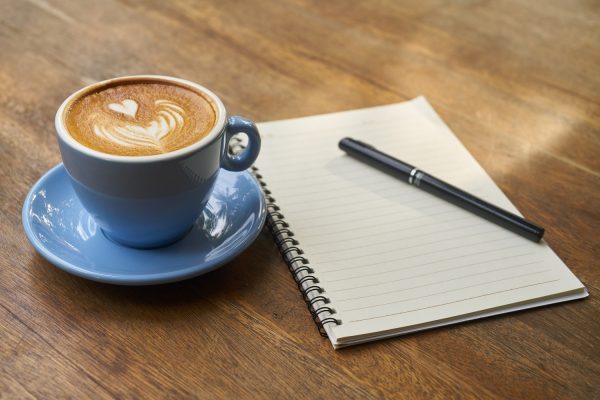 Coffee in a cup and saucer next to a note pad and pen