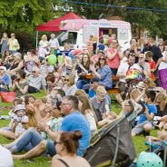 Crowd of people sitting on grass clapping and looking happy.