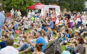 Crowd of people sitting on grass clapping and looking happy.