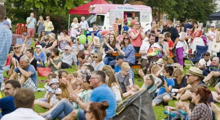 Crowd of people sitting on grass clapping and looking happy.