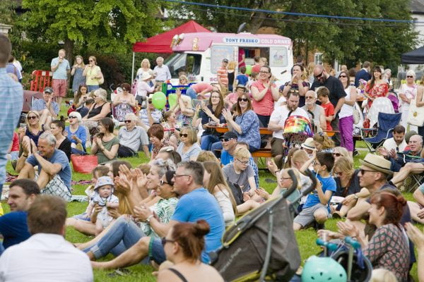 Crowd of people sitting on grass clapping and looking happy.