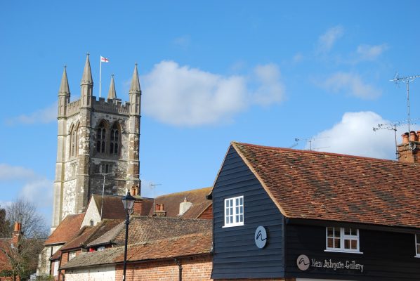 Black timber clad building with rooftops and church behind.