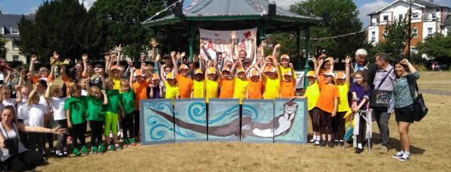 Group of children standing behind a painting of an otter.