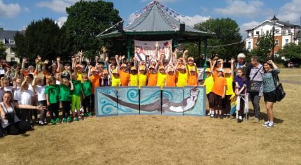 Large group children standing behind a painting of an otter.