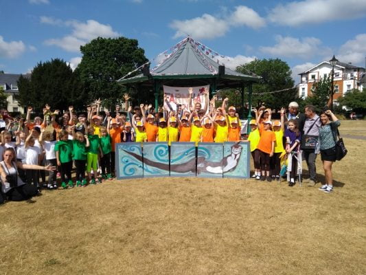 Large group children standing behind a painting of an otter.