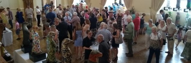 Large group of people standing talking in a hall.