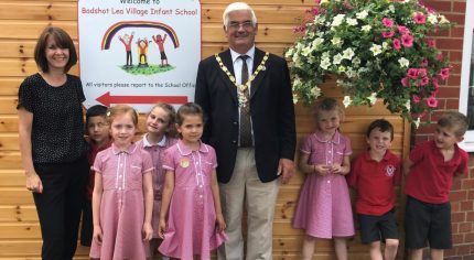 School children and the Mayor stand next to a large hanging basket.