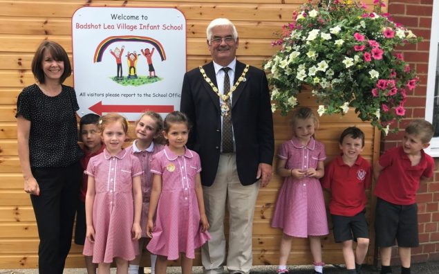 School children and the Mayor stand next to a large hanging basket.