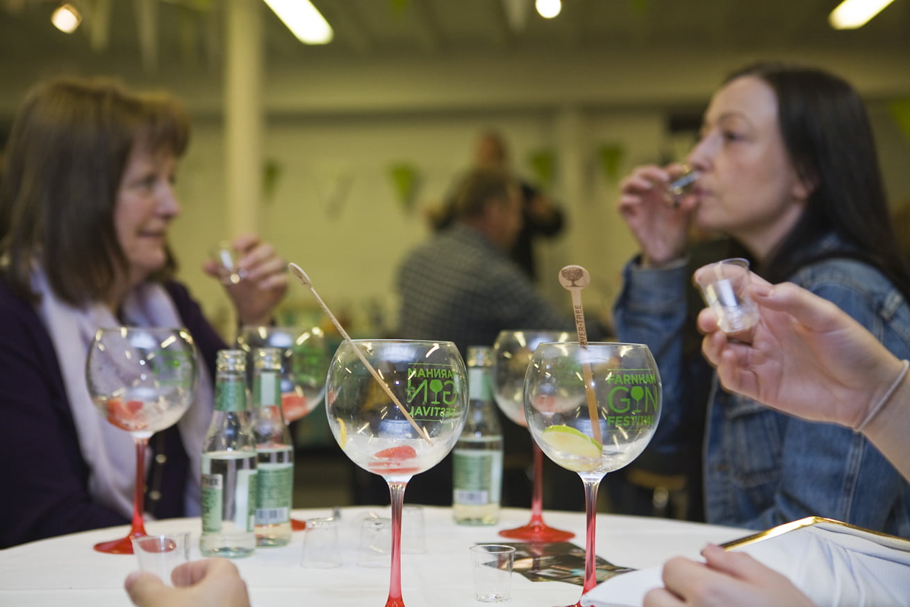 Two females driving from shot glasses and three gin glasses with a red stem