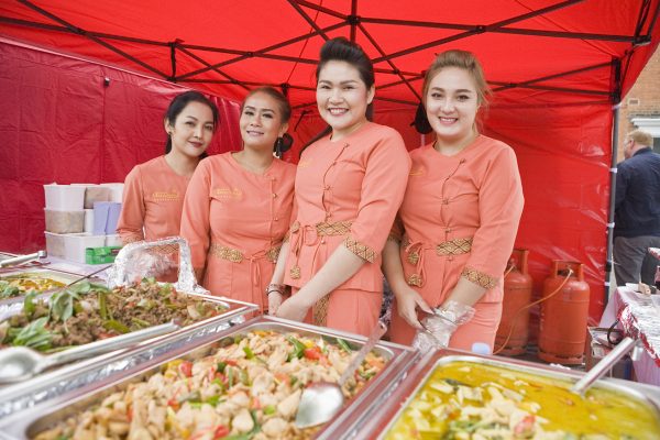 Four females in orange Thai uniforms serving food.